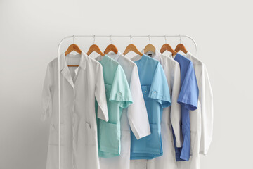 Rack with medical uniform on light background