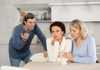 Woman sits near daughter and comforts during quarrel with husband. Mother calms upset daughter takes side of woman in altercation with adult brother. Man is outraged by girlfriend behavior and blames