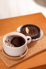 Cup of coffee with coaster and cake on table in room, closeup