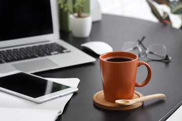 Cup of coffee with wooden coaster and spoon on desk in office, closeup