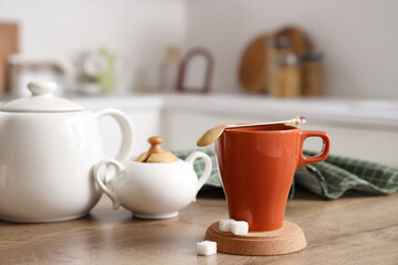 Cup of tea with spoon, coaster and sugar on table in kitchen, closeup