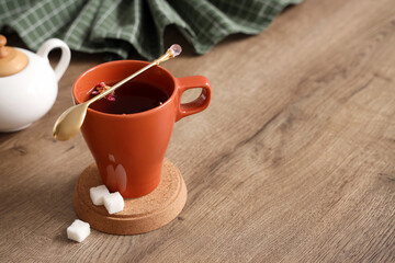 Cup of hibiscus tea with spoon, coaster and sugar on table in kitchen, closeup