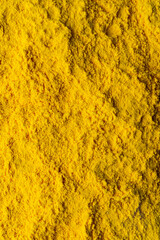 Golden turmeric powder sprawls across a textured wooden surface, highlighting its vivid hue. The scene captures the essence of spices and natural colors in a cozy kitchen environment