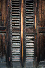 Close-up of aged dark wooden shutters with deep texture, golden central grain, and subtle metal...