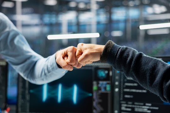 Close up of admins doing fist bump in data center after successfully optimizing performance with AI assistant. Data center IT experts celebrating good results, speeding up tasks with LLM chatbot