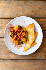 Bright colors fill the plate with a flavorful dish topped with herbs and chickpeas, complemented by golden, crispy tortillas, all resting on warm, rustic wood