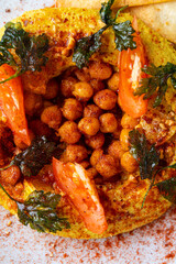 Brightly colored chickpeas are artistically arranged and topped with fresh herbs and tomatoes, showcasing a lively and flavorful dish perfect for sharing at gatherings or meals