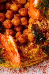 A colorful dish showcases chickpeas seasoned perfectly with spices, garnished with sliced tomatoes and fresh herbs. Enjoyed at a lively eatery during lunchtime, this meal is warm and inviting