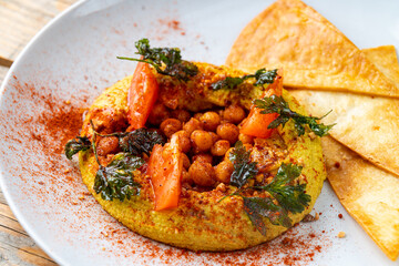 Bright and colorful dish features spiced chickpeas garnished with fresh herbs and tomatoes, alongside crispy tortilla chips, enjoyed at an outdoor market during midday