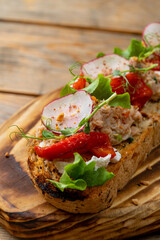 A colorful open-faced sandwich showcases a delightful mix of crisp lettuce, roasted red peppers, and creamy tuna salad on toasted bread. This appetizing dish is served on a rustic wooden board