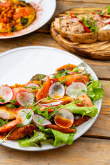 Colorful salad featuring grilled chicken, fresh veggies, and crispy lettuce is served on a wooden table. Nearby dishes add to the inviting atmosphere of a sunny afternoon meal