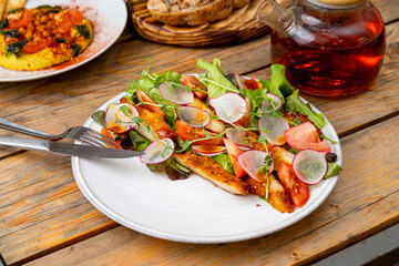Crispy chicken topped with fresh greens, sliced tomatoes, and radishes sits beautifully on a rustic plate. Warm ambiance surrounds a delightful meal, perfect for sharing