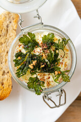 A delightful jar filled with creamy goodness is topped with crispy greens and sprinkled with nuts. It is served alongside a slice of rustic, freshly baked bread