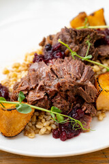 Tender beef is nestled alongside roasted root vegetables and cranberries atop a hearty grain base. The dish is beautifully arranged with fresh greens, creating a mouthwatering experience