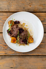 A delightful dish of tender, slow-cooked meat rests on a bed of grains, accompanied by roasted pear slices and a sweet berry sauce, creating a feast for the senses