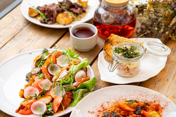 A vibrant brunch table displays an array of dishes including fresh salads, savory meats, and aromatic tea. The inviting atmosphere promises a delightful culinary experience