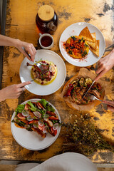 Friends gather around a rustic wooden table, enjoying a colorful display of dishes. Plates feature fresh ingredients, showcasing vibrant flavors and textures in a cozy setting