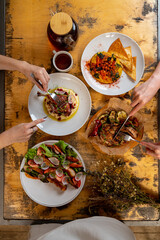 Friends share a lively meal at a rustic wooden table, filled with colorful dishes and enticing aromas. Each person eagerly enjoys the diverse flavors and textures of their meals