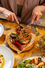 A person is savoring a beautifully grilled piece of meat accompanied by colorful roasted vegetables. Sunlight streams into the cozy eatery, creating a warm atmosphere