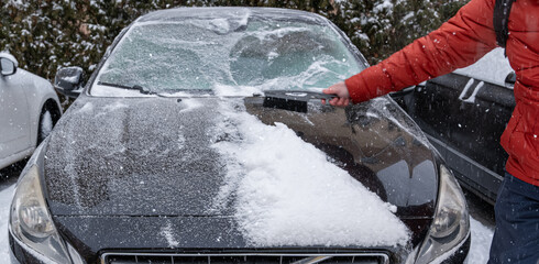 Clearing snow from car hood during winter snowfall