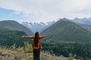 Obraz premium Person standing on a mountain overlook with arms wide, embracing vast valley and snowy peaks, conveying freedom, adventure, and connection with nature.