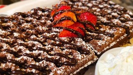 Chocolate waffles dusted with sugar, topped with strawberries and drizzled with chocolate, served with whipped cream.