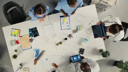 Obraz premium Top down view of physicians and medics gathered for briefing conference. Group discusses healthcare advancements, laboratory research and treatment methods to enhance medical care.