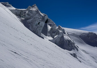 Dramatic icy rock formations and a steep snowy slope on a high-altitude glacier in the swiss Alps under a deep blue sky. A striking winter landscape with rugged natural textures.