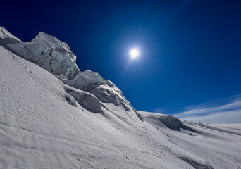 Snowy Alpine ridge with sharp ice formations under a deep blue sky in bright winter sunlight. High-altitutde landscape showcasing rugged textures and prisitine mountain scenery.