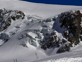 Snowy glacier landscape with dramatic rocky ridges in the Swiss Alps near Zermatt. Winter mountain scenery captured in bright sunlight