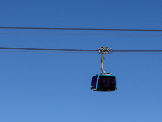 Minimalist view of a cable car cabin hanging on a ski lift line against a deep blue winter sky in the Alps, capturing clean lines, calm atmosphere, and alpine transportation.