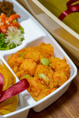Kentang balado, a traditional Indonesian dish made from spicy chili-coated potatoes, served in a white compartment meal box. Vibrant red-orange seasoning and chunky texture.