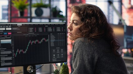 Businesswoman studies financial charts using stock market visualization tools. Digital trading platform provides economic data, forex analysis and price trends for investment planning. Camera B.