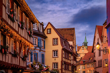 Fototapeta premium Christmas decorations on half timbered houses in Colmar, France glow at sunset