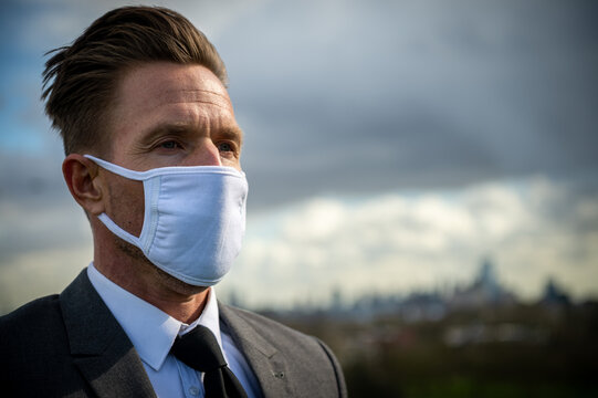 Businessman in a suit wearing a face mask with a dark clouds looming over a city skyline - Powered by Adobe