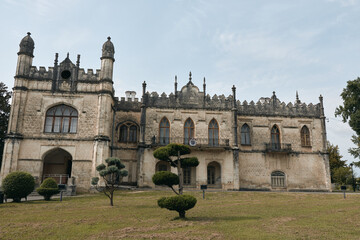 Historic castle style building with towers and stone facade on a well kept lawn, trimmed trees and blue sky, showcasing grand architecture and timeless exterior landscape