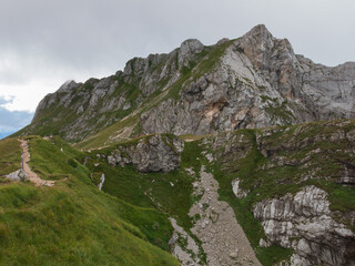 Epic alpine mountains landscape of the Mangart massive rugged cliffs with atmospheric light from the cloudy sky 