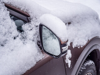 Snow-covered car side mirror and windows in close-up, captured in realistic style on a snowy outdoor background, depicting winter season