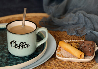 Cozy coffee break with sweet treats. creamy coffee in a mug with spoon, wafer roll and chocolate cookie, warm home atmosphere and dessert flavors concept. home comfort and morning coffee ritual
