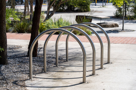 A stainless steel bicycle rack in a landscaped public space, featuring curved metal arches set on a paved surface. Concept of urban transport amenities, cycling infrastructure in Australia.