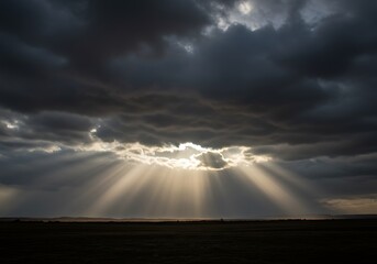 Dramatic sky with sun rays piercing through clouds over a dark landscape