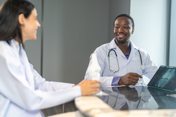 Diverse medical team african male doctor and female doctor collaborating and reviewing medical documents writing and discussing patient data in hospital office, teamwork in healthcare, patient care