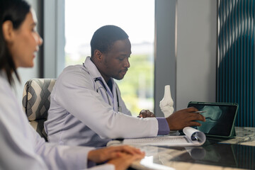 Diverse medical team african male doctor and female doctor collaborating and reviewing medical documents writing and discussing patient data in hospital office, teamwork in healthcare, patient care