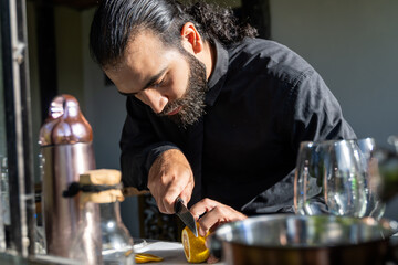 Bartender slicing lemon in hotel bar with cocktail tools and warm light.