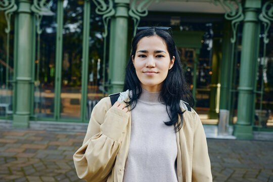 Woman outdoors in casual clothing near green architectural columns in daytime urban setting, calm expression, street style and confident vibe, approachable appearance