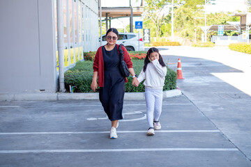 A mother and daughter walking together through a parking lot, holding hands and enjoying a bright...