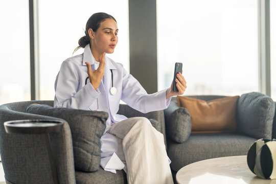 Female doctor using smartphone for remote work, conducting video call consultation to provide health advice and telemedicine services for patient, online medical care, diagnosis and treatment