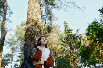 Forest, woman leaning against a tall tree, gazing upward in a serene moment of nature, outdoor...
