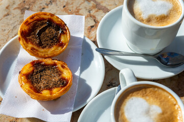 Traditional Portuguese breakfast snack of Pastel de Nata (custard tart) and coffees on a marble...
