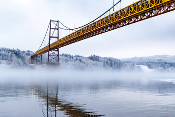 Obraz premium Steel and concrete bridge across the foggy river in winter.